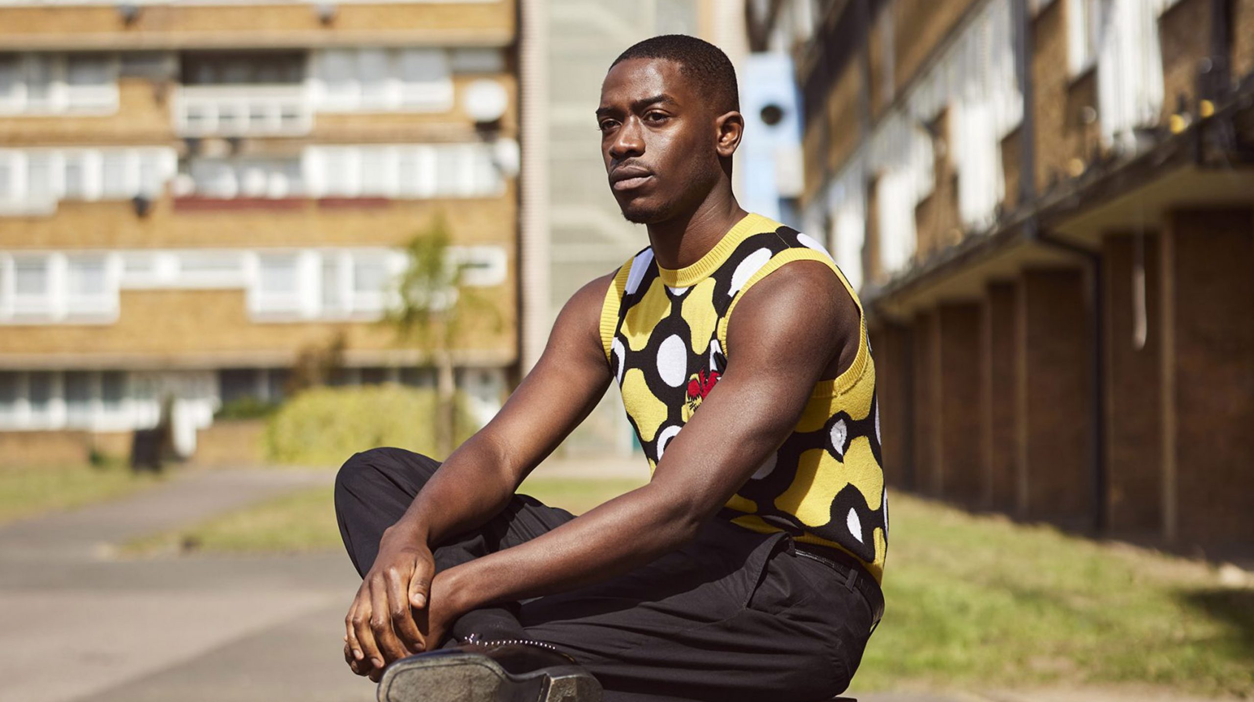 Damson Idris sitting cross legged in front of an apartment block