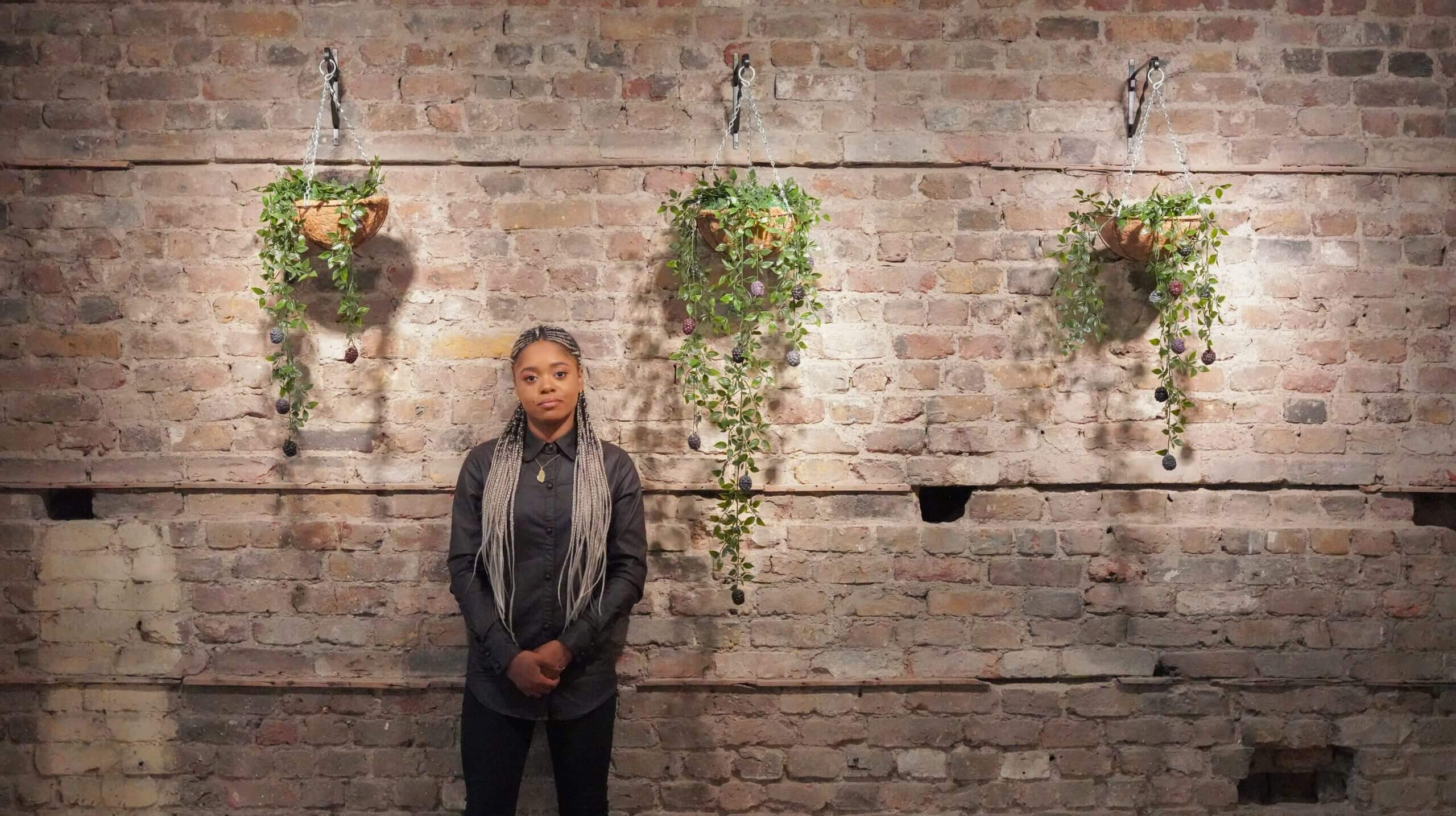 Lauren Marie Haywood beside some of her handmade plant artwork mounted on a brick wall