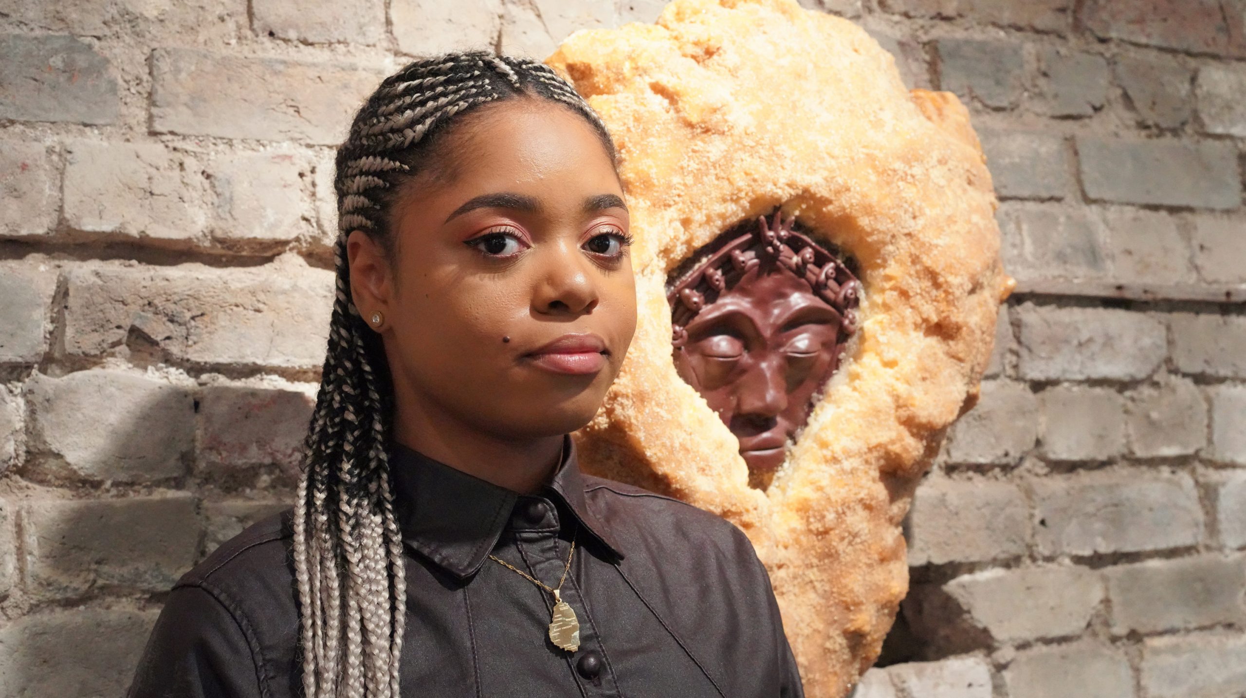 Lauren Marie Haywood beside some of her handmade artwork mounted on a brick wall