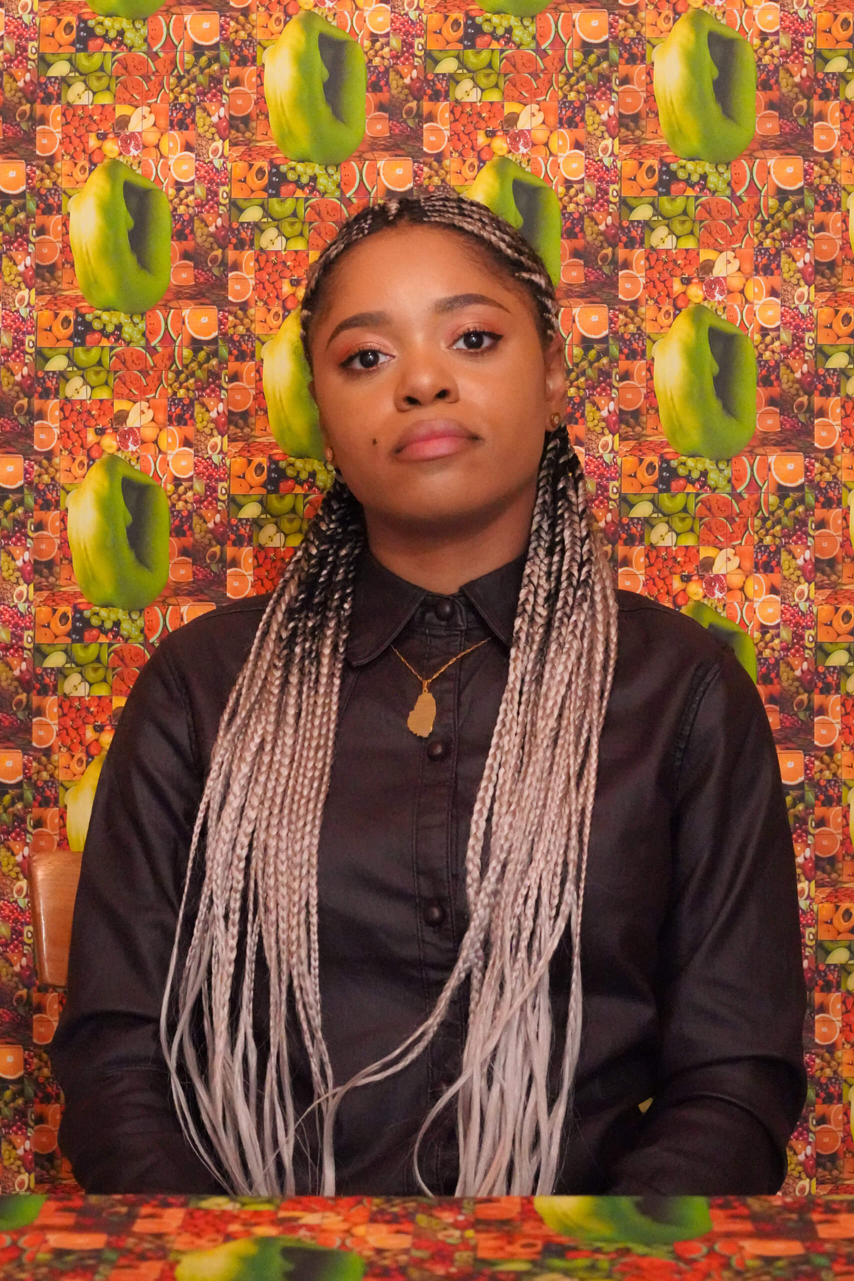 Lauren Marie Haywood looking at the camera while sitting in a room with brightly coloured fruit wallpaper