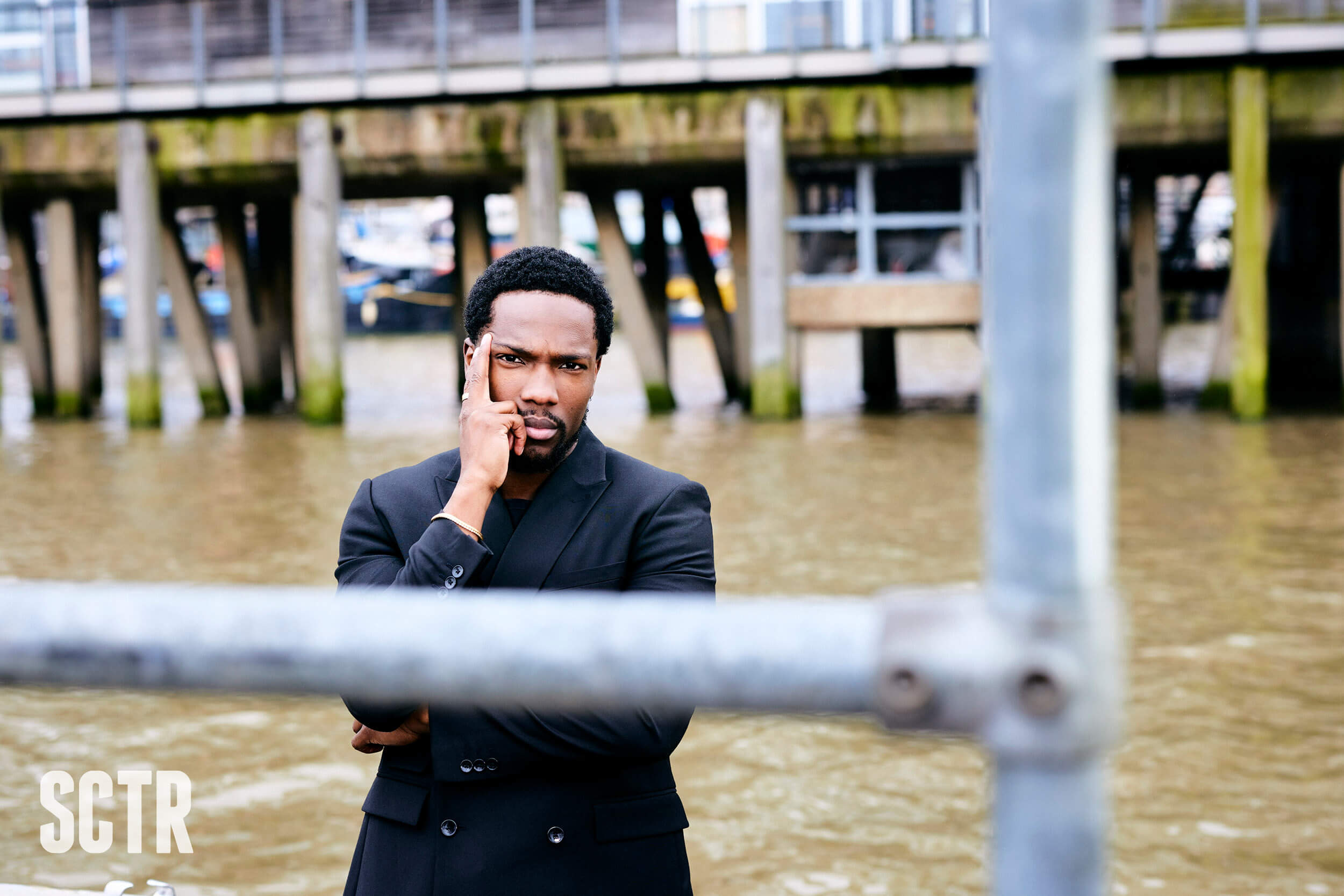 Tosin Cole standing by the water with his hand to his cheek