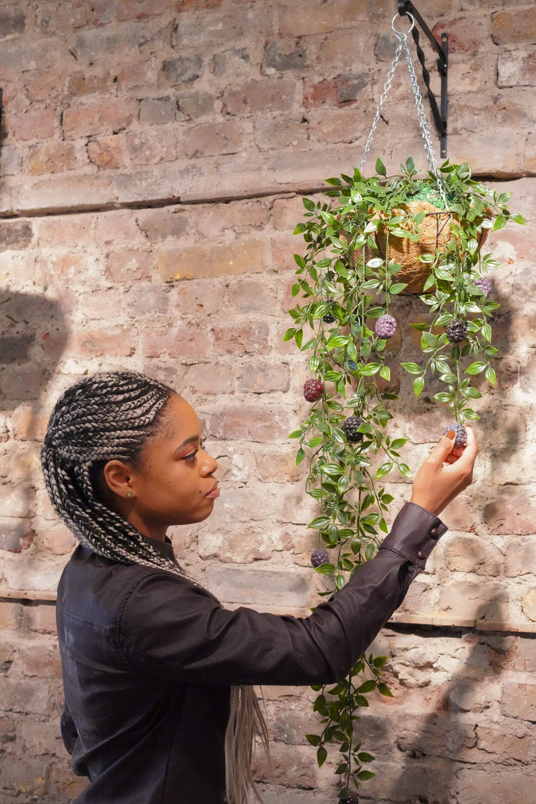 Lauren Marie Haywood beside some of her handmade plant artwork mounted on a brick wall