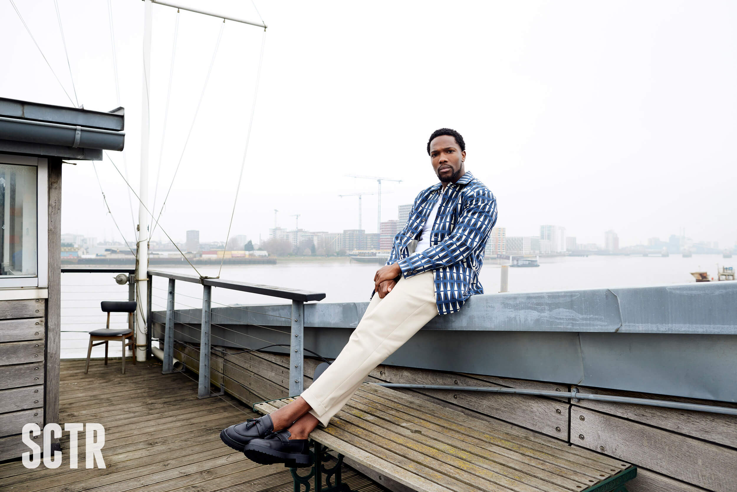 Tosin Cole sitting on a wall by a dock